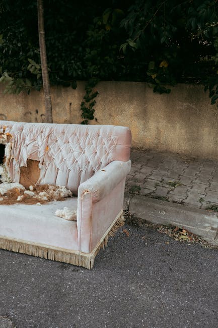Three individuals are involved in moving a large flat-packed piece of furniture, possibly a table or bed frame, along a city sidewalk. The object has a wooden frame with visible light-colored timber s